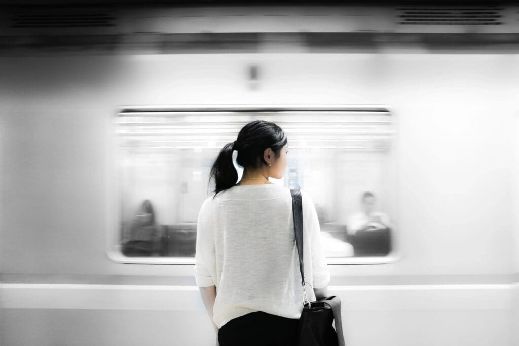 Woman waiting at subway platform as train passes by in motion blur.