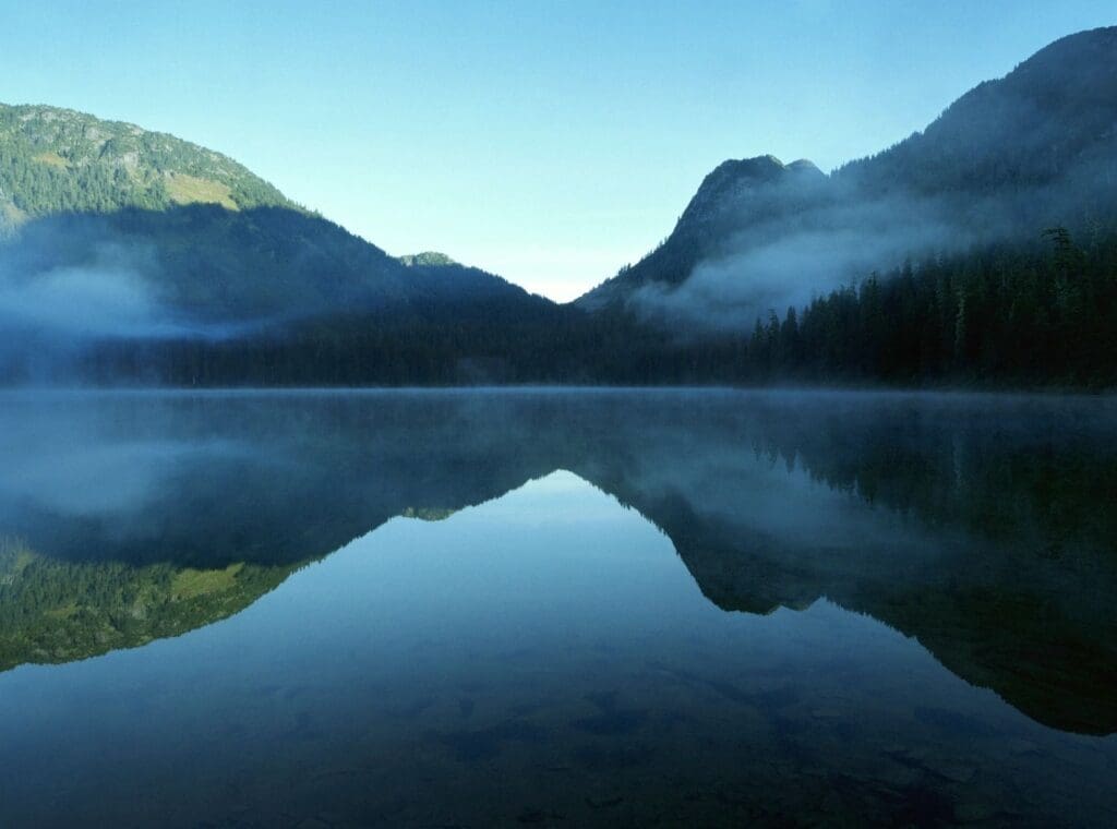 Serene lake reflecting mountains and clear blue sky.