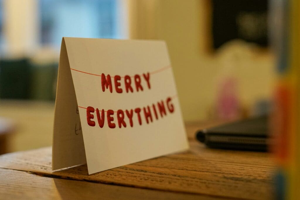 A holiday card with 'Merry Everything' on a wooden surface.